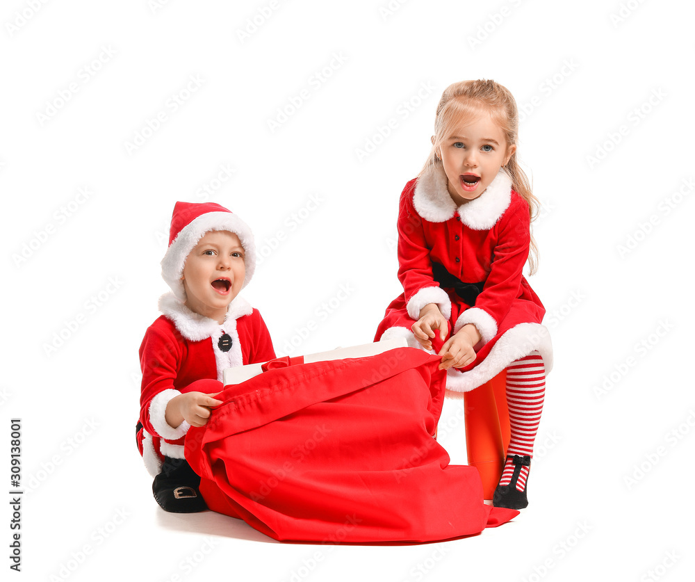 Cute little children in Santa costumes and with bag full of gifts on white background