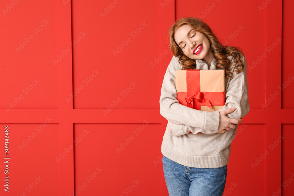 Happy young woman in winter clothes and with Christmas gift on color background