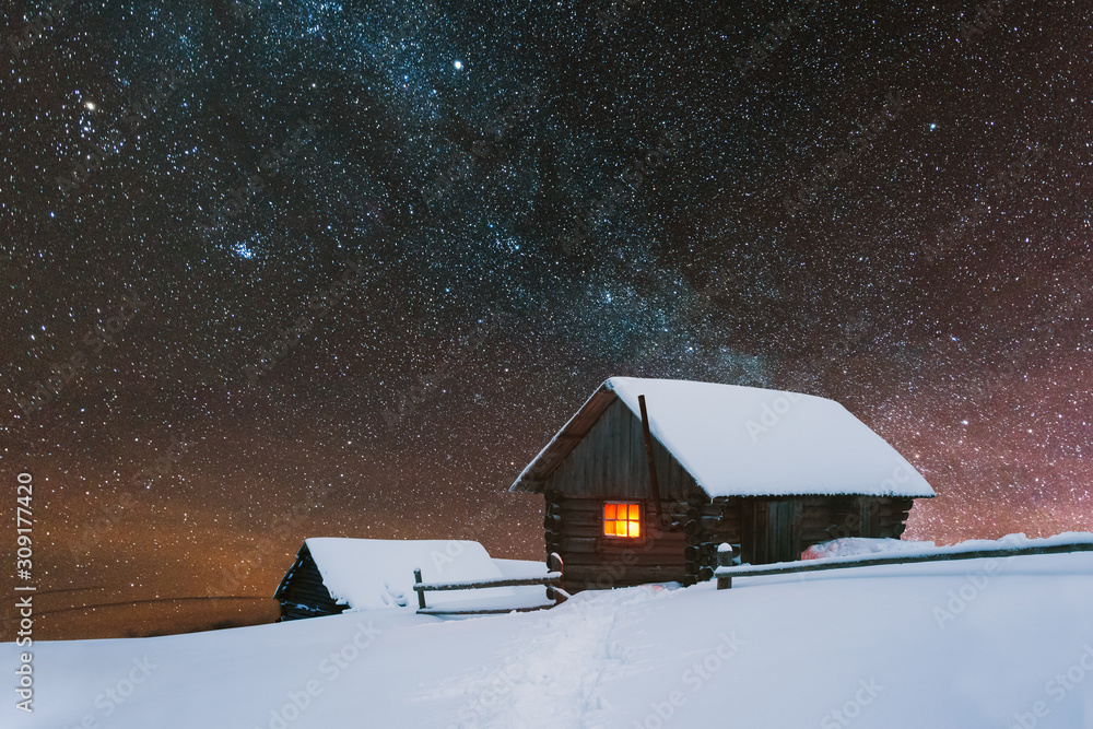 戏剧性的冬季场景，窗户里有温暖的灯光，有雪房子。奇妙的夜景闪闪发光