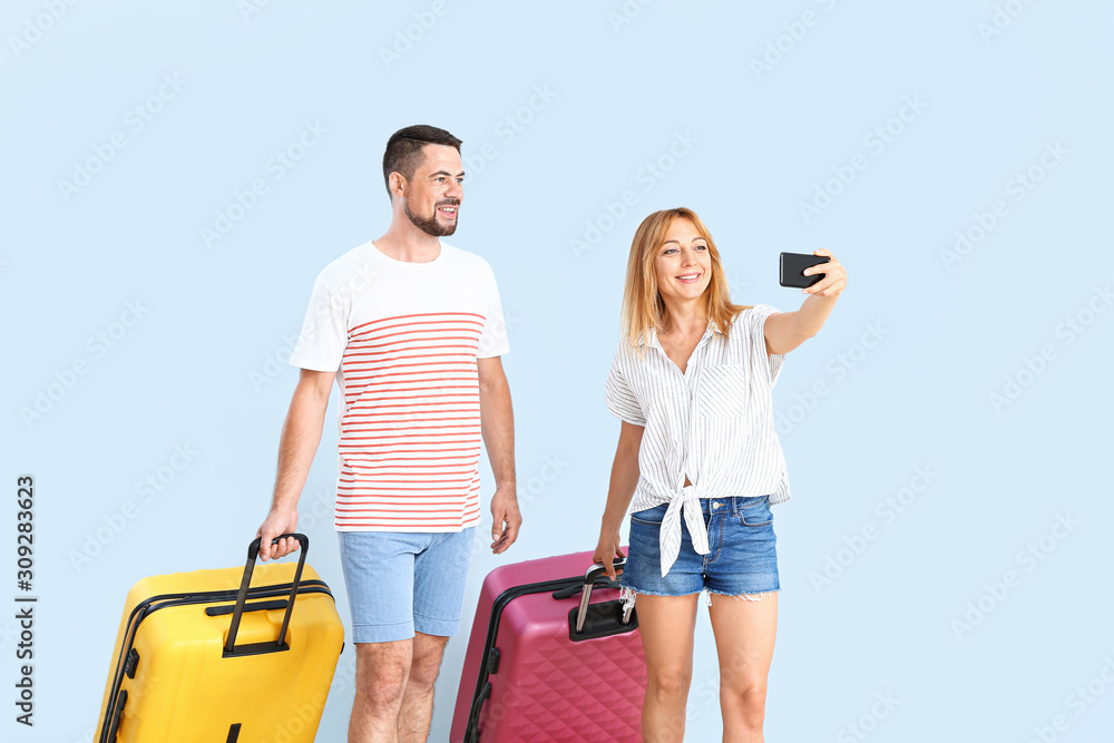 Couple with suitcases taking selfie on color background