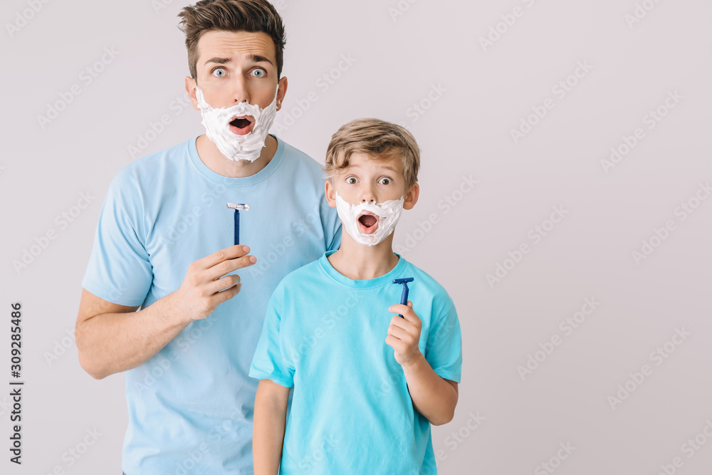 Funny father and his little son shaving against grey background