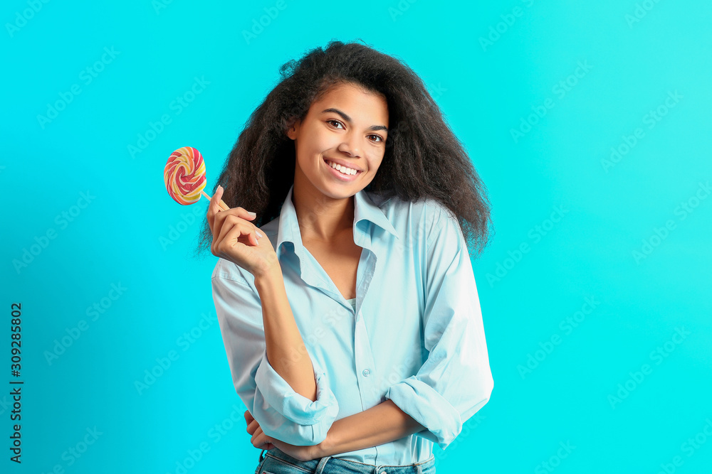 Happy African-American woman with tasty lollipop on color background