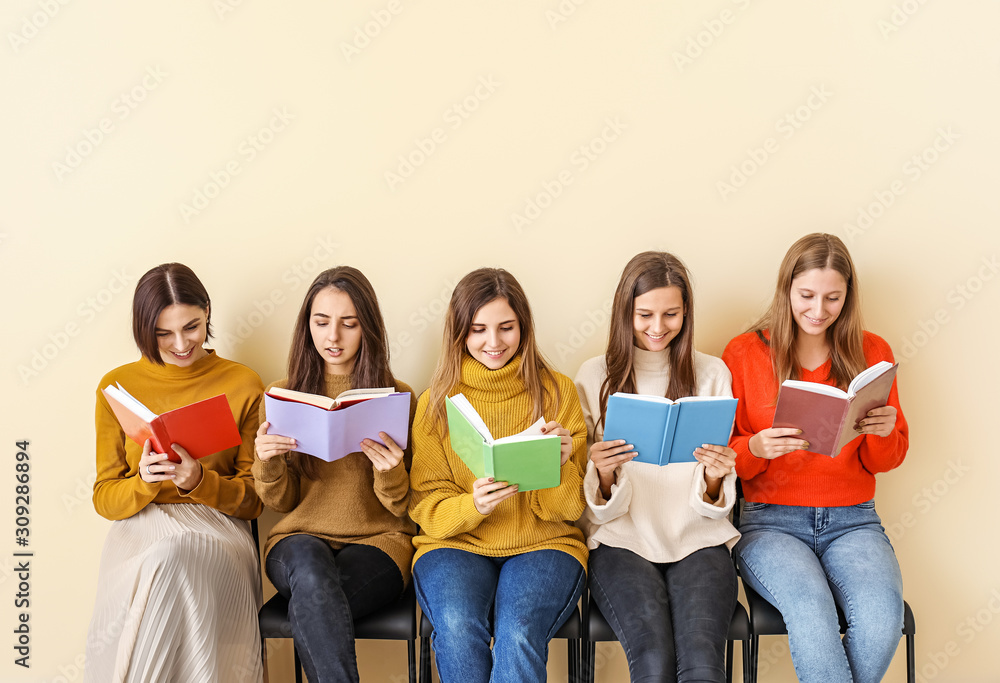 Young women with books sitting near color wall