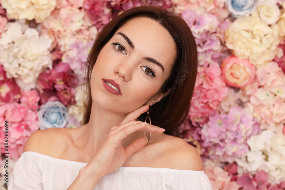 Portrait of beautiful young woman near wall made of flowers