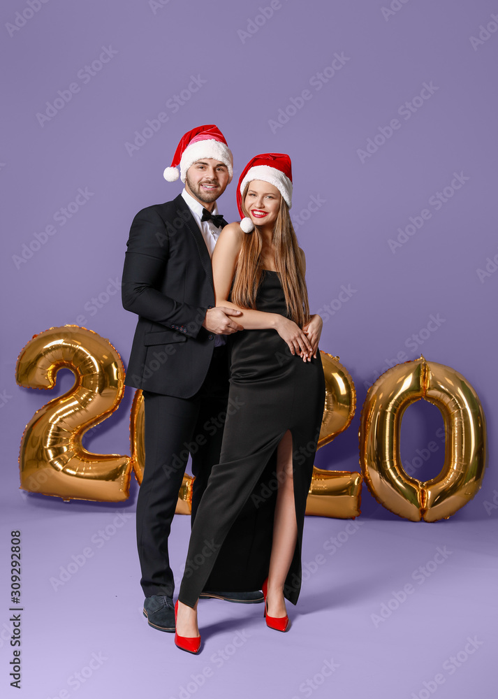 Happy couple in Santa Claus hats on color background