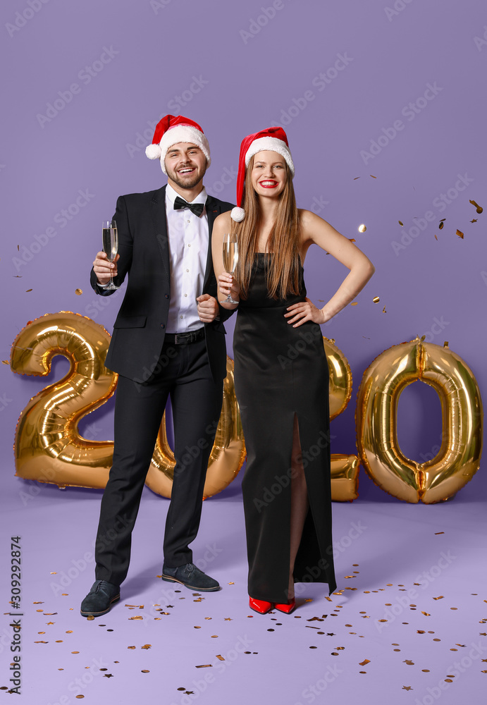 Happy couple in Santa Claus hats and with glasses of champagne on color background