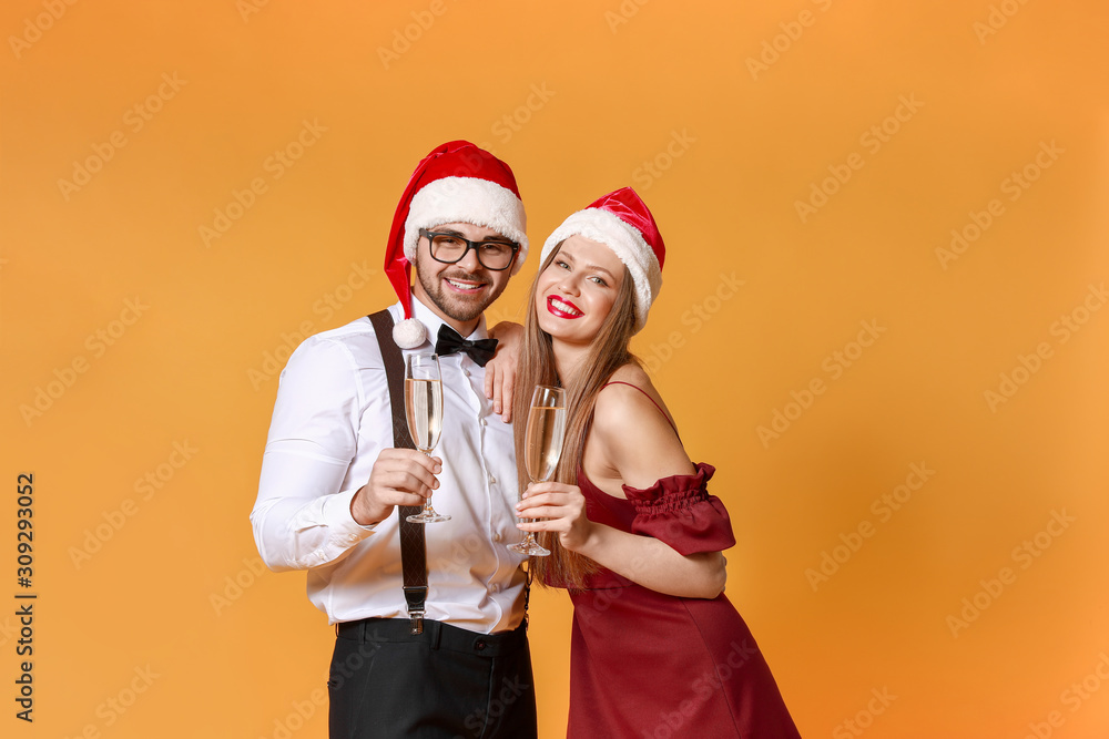 Happy young couple in Santa Claus hats and with glasses of champagne on color background