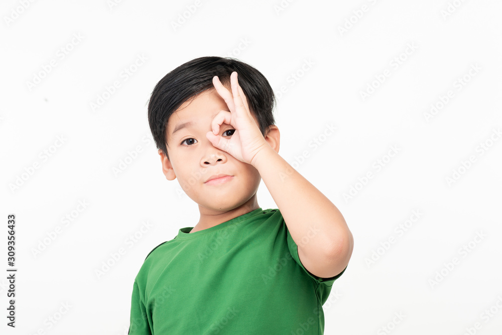 Dark haired little child with happy face smiling doing ok sign with hand on eye looking through fing