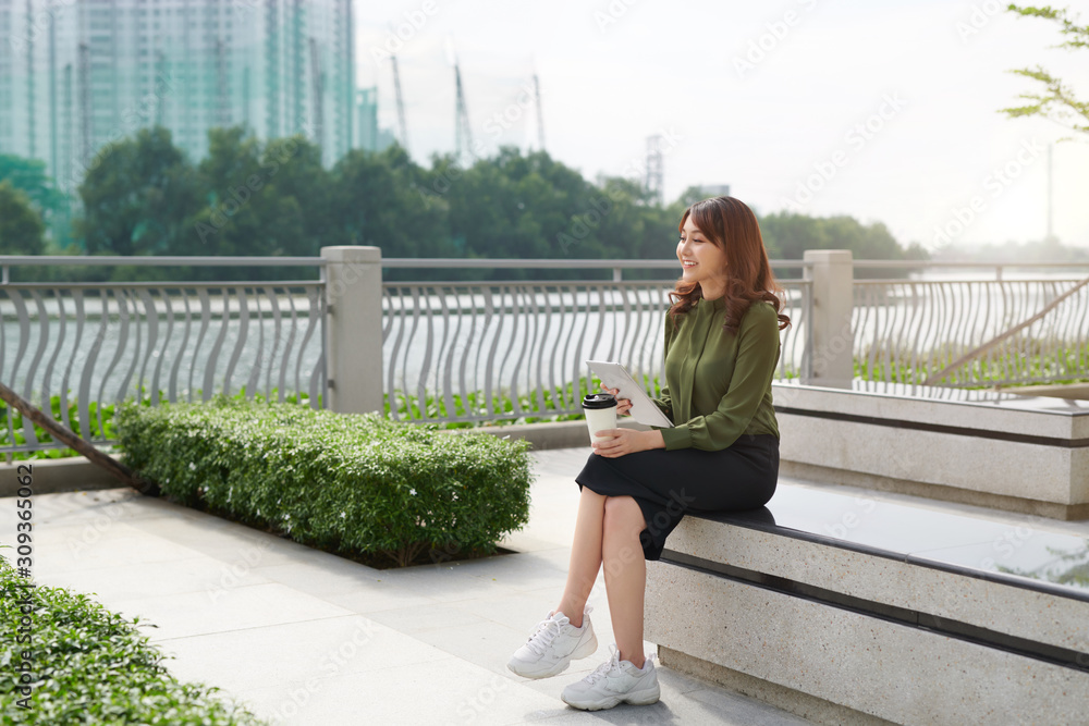 亚洲年轻女子在长椅公园上网玩平板电脑