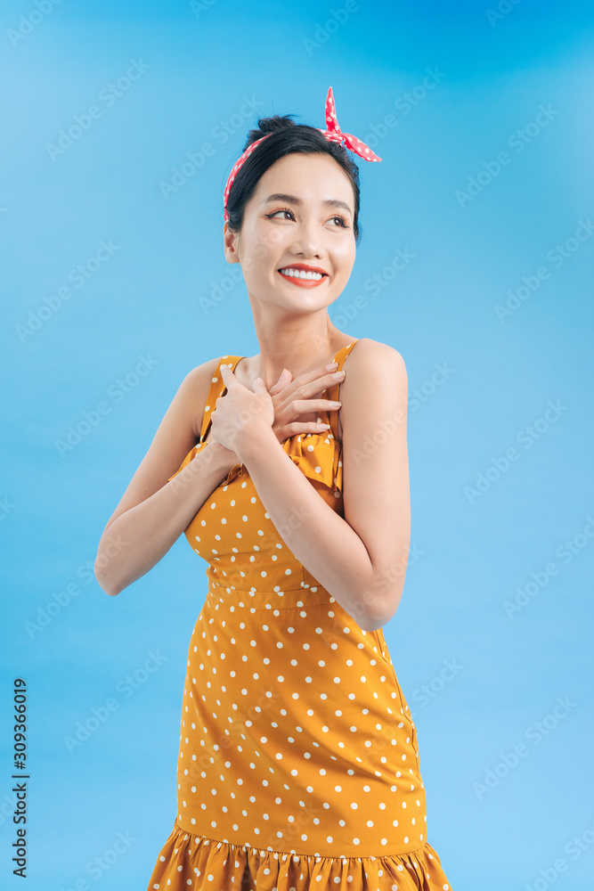 Beautiful young woman in polka dot dress is standing, looking away and smiling