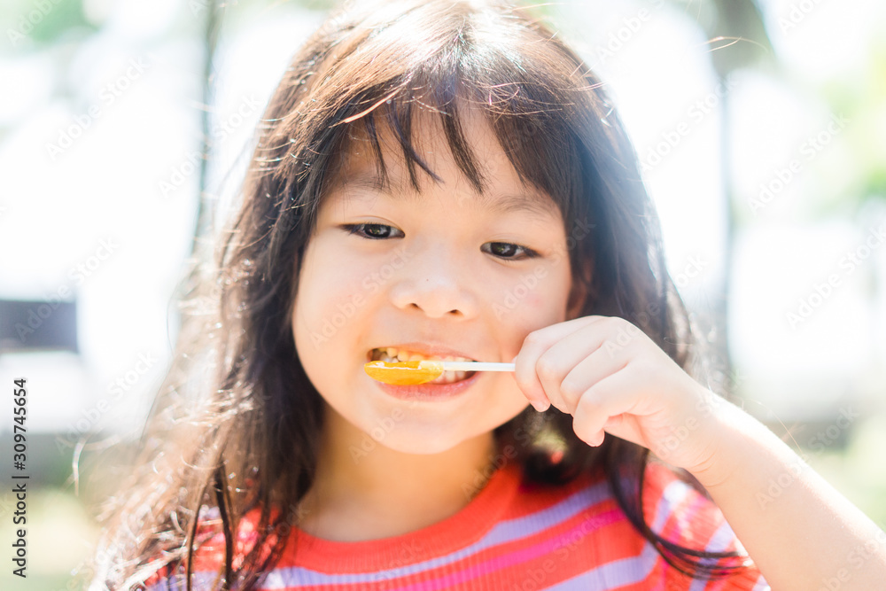 Happy 5 years old asian girl with a lollipop on a sunny day in the garden at home.Happy and Deliciou