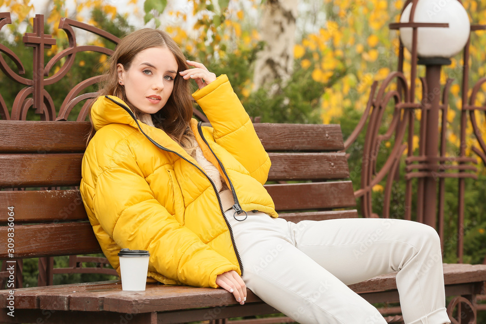 Portrait of stylish young woman with cup of coffee on autumn day