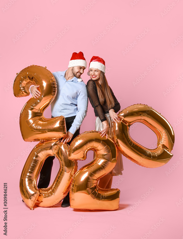 Happy couple in Santa Claus hats and with air balloons on color background