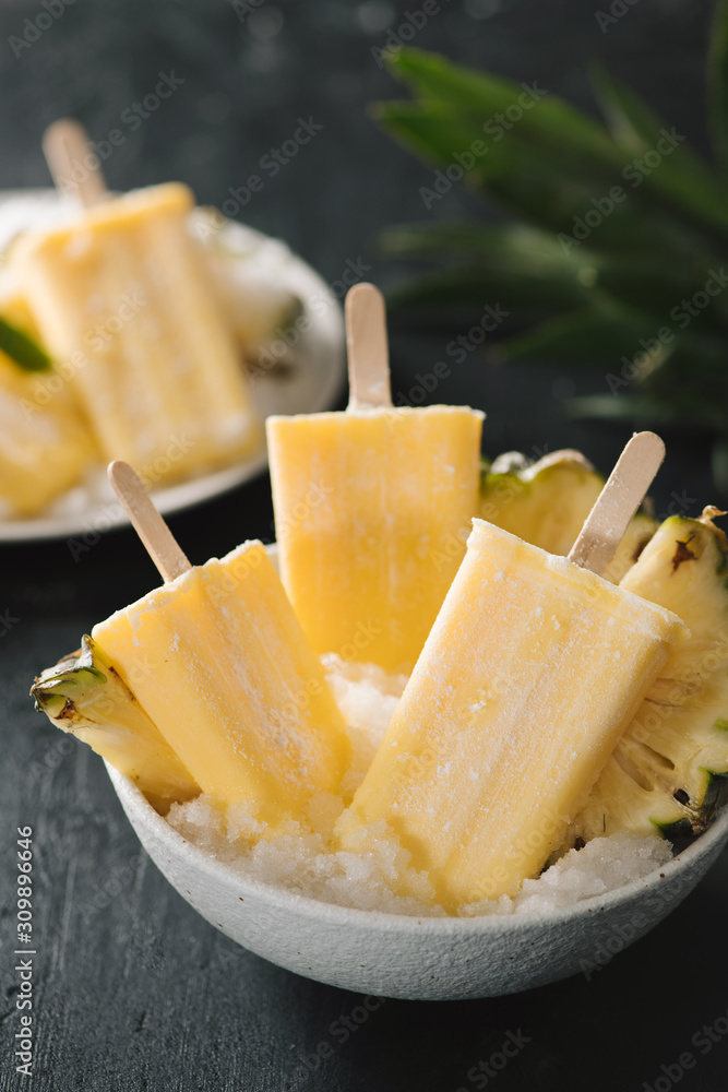 Overhead view of yellow ice lollies inverted in a white bowl on dark table