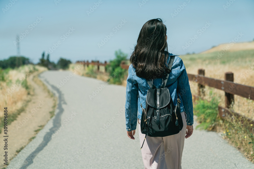 亚洲女旅行者在阳光照射下的蓝天下，在户外草地上愉快放松的背影。