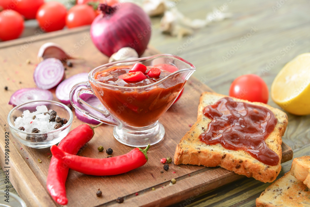 Gravy boat with barbecue sauce, toasted bread and spices on wooden table