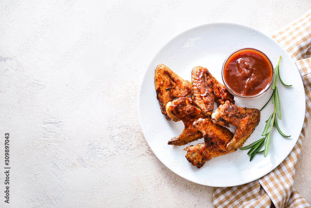 Plate with tasty fried chicken wings and barbecue sauce on white table