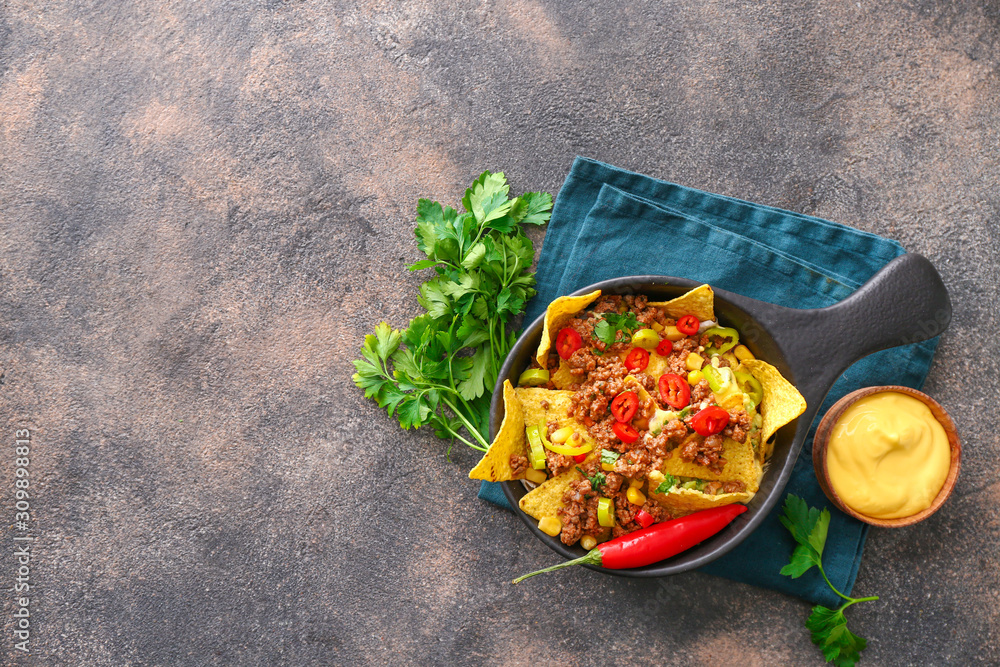 Frying pan with tasty chili con carne and nachos on grey background