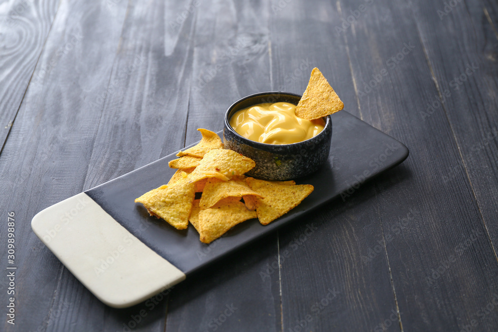 Board with tasty nachos and sauce on dark table