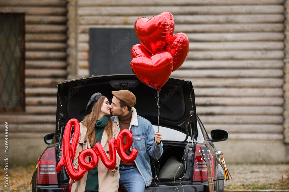 Happy young couple with car and air balloons outdoors. Valentines Day celebration