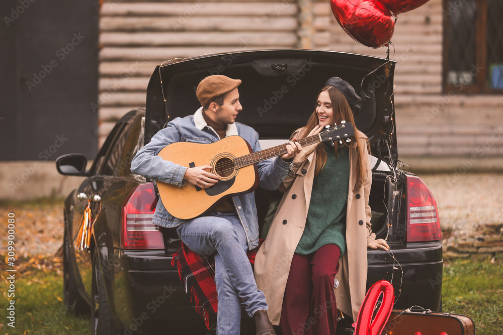 Happy young couple with car and guitar resting in park. Valentines Day celebration