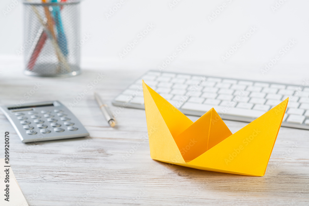 Workspace with office desk and yellow paper ship