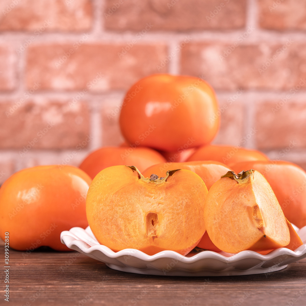 Fresh beautiful sliced sweet persimmon kaki on dark wooden table with red brick wall background, Chi