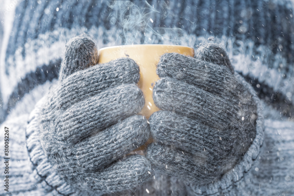 Girl in mittens holds a cup of hot tea in the snow