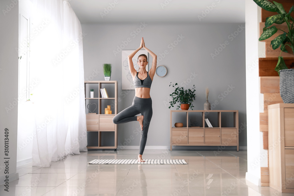 Beautiful young woman practicing yoga at home