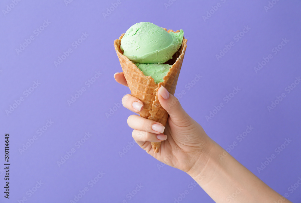 Female hand with sweet ice-cream on color background