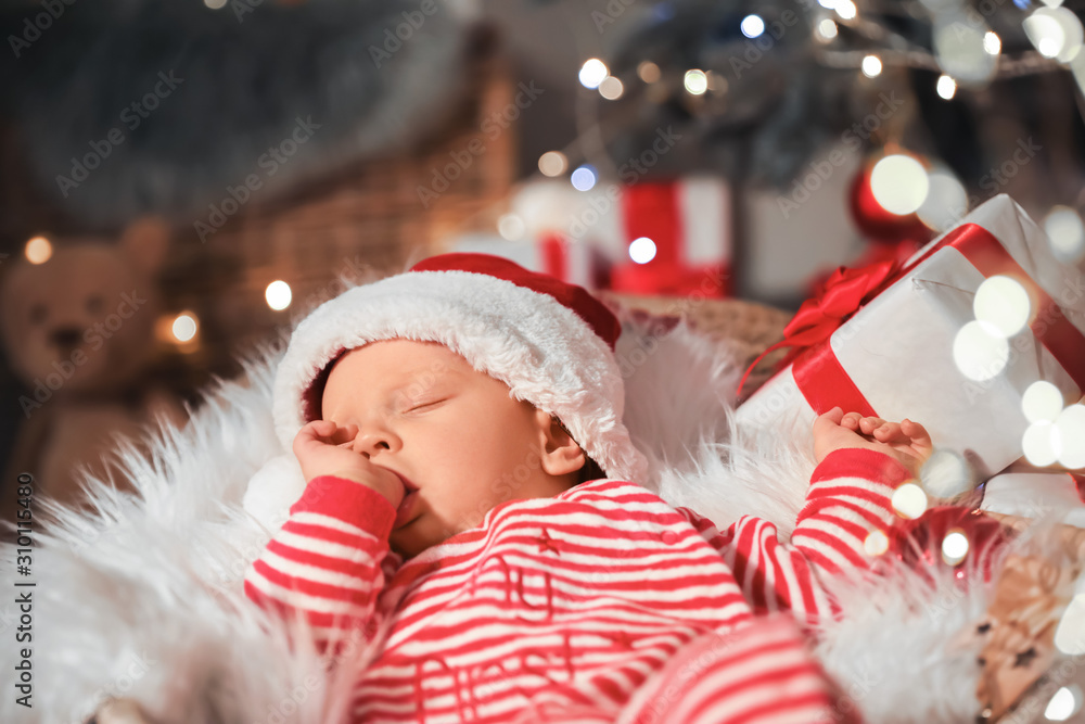 Cute little baby with Santa Claus hat and Christmas gift sleeping in basket at home