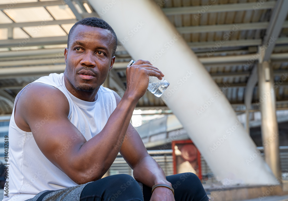 African sportsman drinking water from bottle looking far away with thoughtful face expression,People