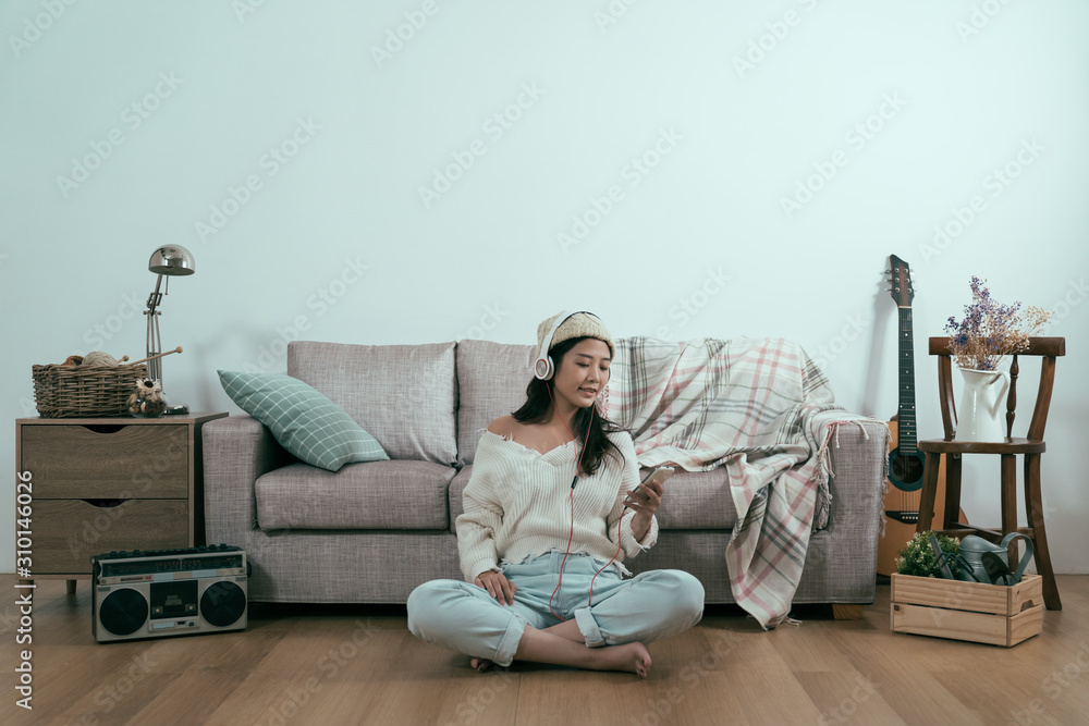 Young charming asian woman sitting on living room floor listening to the music in headset relaxing a