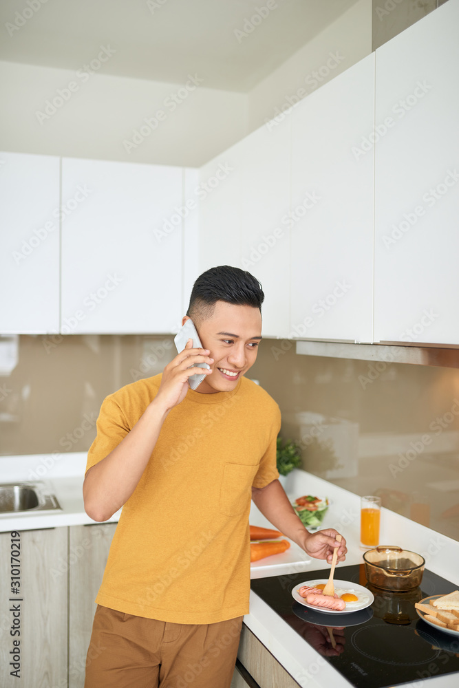 Handsome bachelor 30s talking on mobile phone, while having breakfast in morning