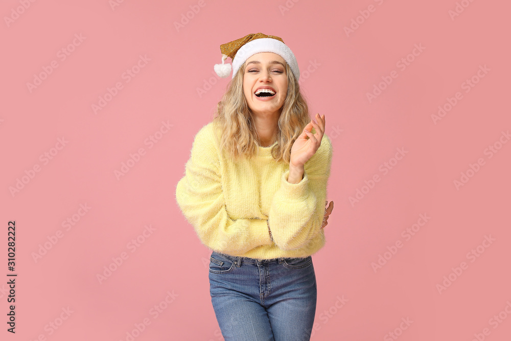 Happy young woman in winter clothes and Santa Claus hat on color background