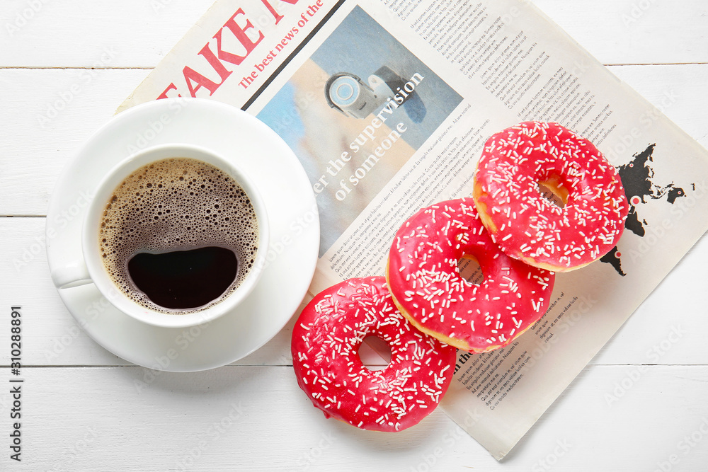 Sweet tasty donuts, cup of coffee and newspaper on white wooden background