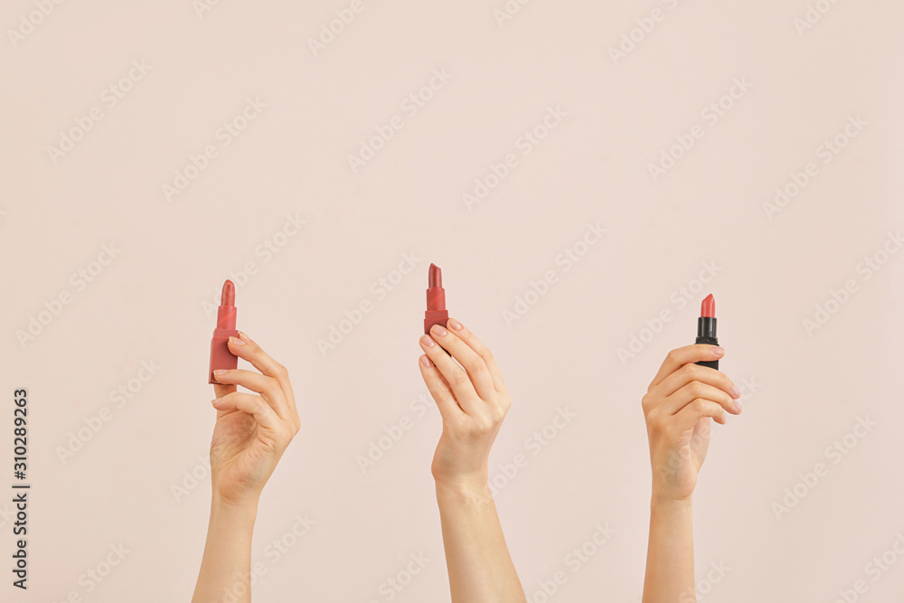 Female hands with lipsticks on color background