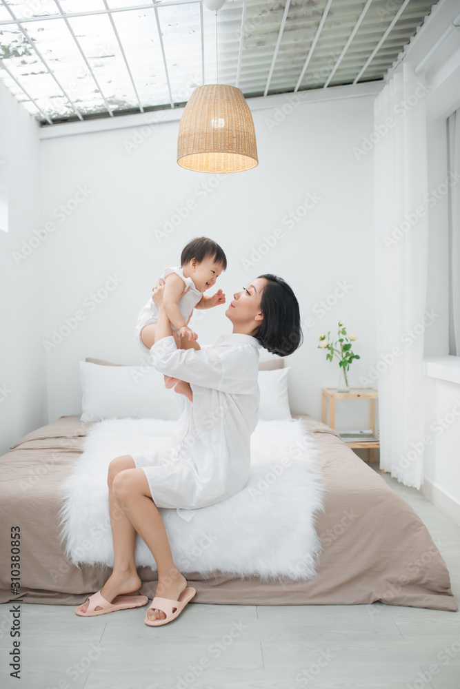 Portrait of happy young mother with baby in bedroom