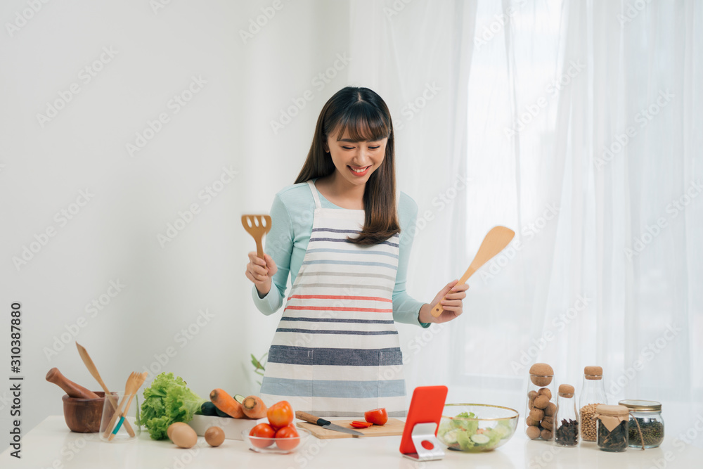 漂亮的年轻亚洲女人一边做沙拉一边看烹饪食谱或看节目