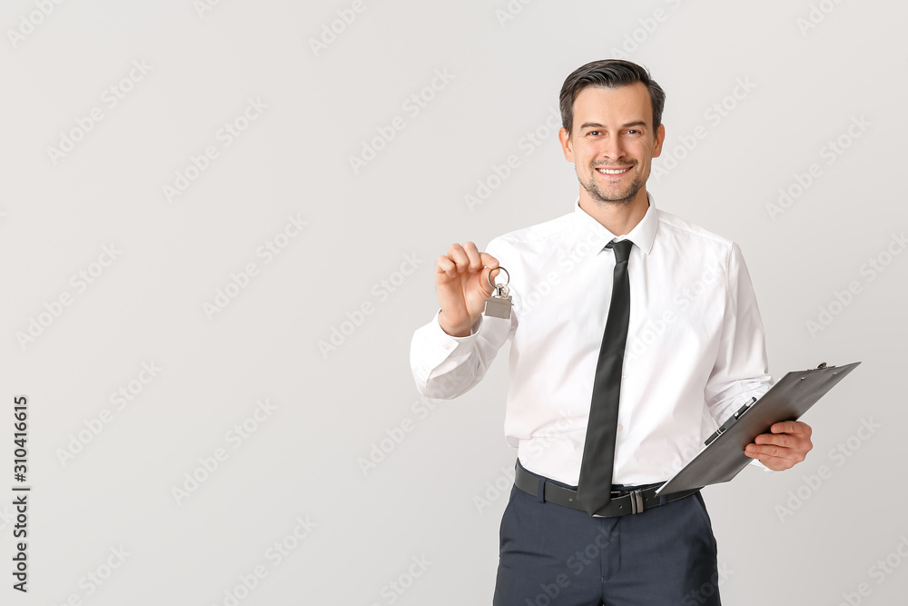 Male real estate agent with key on light background