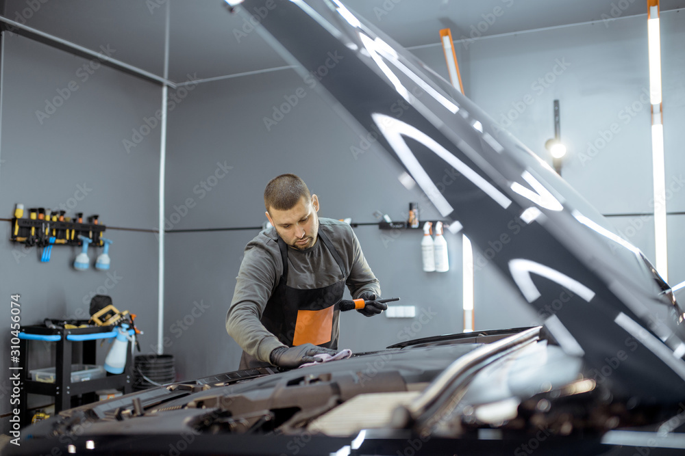 Service worker in uniform performs a professional car cleaning, wiping engine at the vehicle service