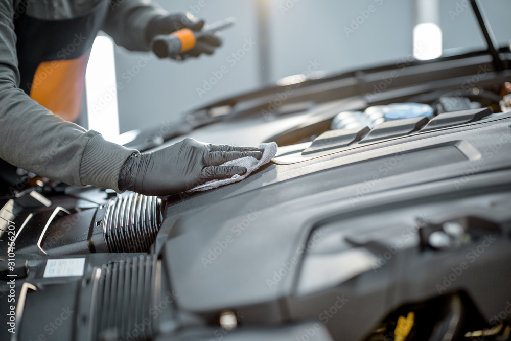 Man performs a professional car cleaning, wiping engine with microfibre at the service station, clos