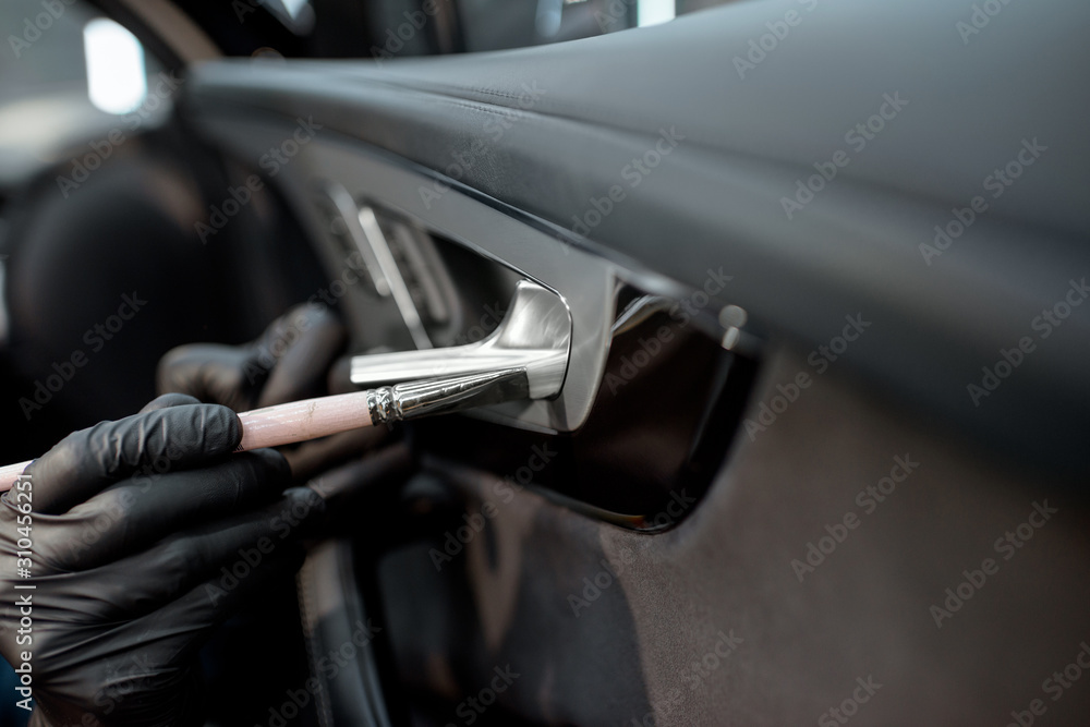 Worker provides a professional vehicle interior cleaning, wiping door panel with a brush at the car 