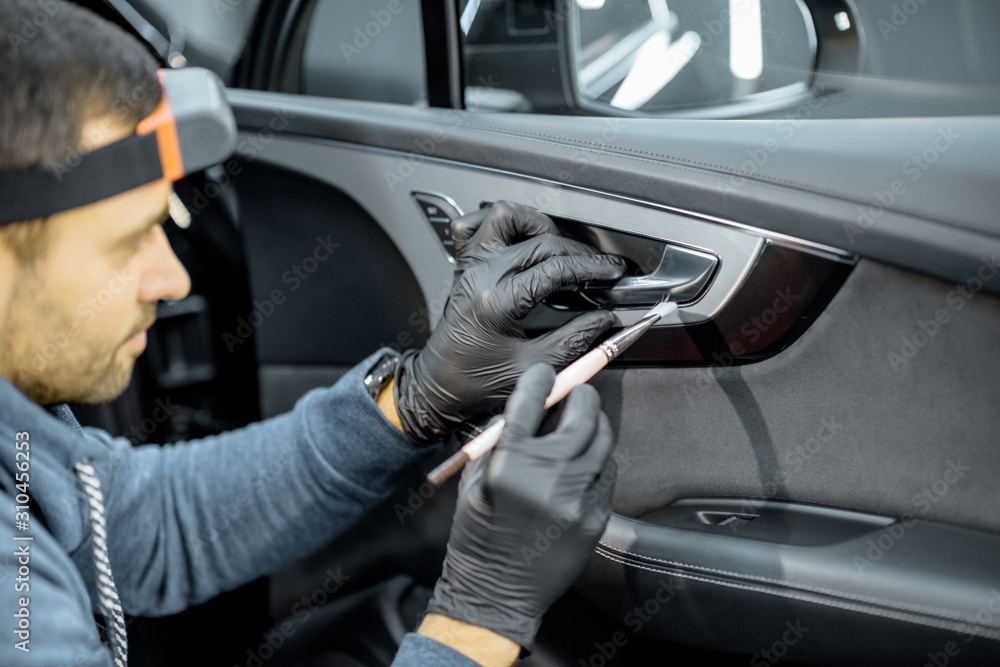 Car service worker in uniform provides a professional vehicle interior cleaning, wiping door panel w