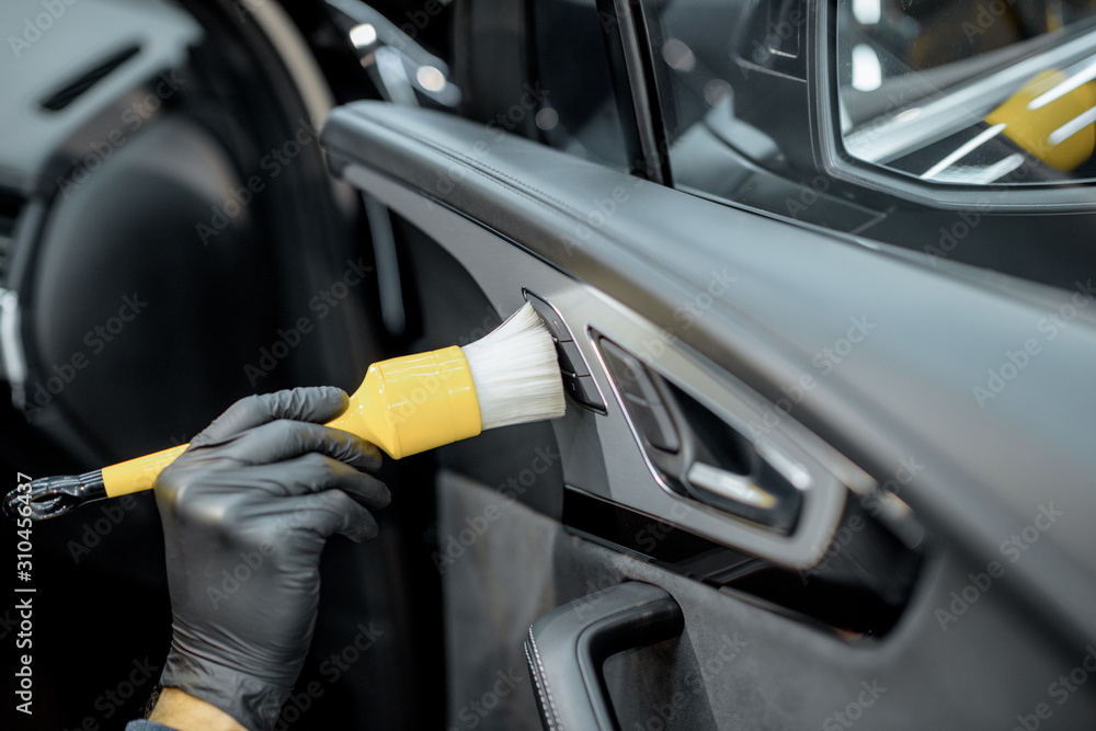 Worker provides a professional vehicle interior cleaning, wiping door panel with a brush at the car 