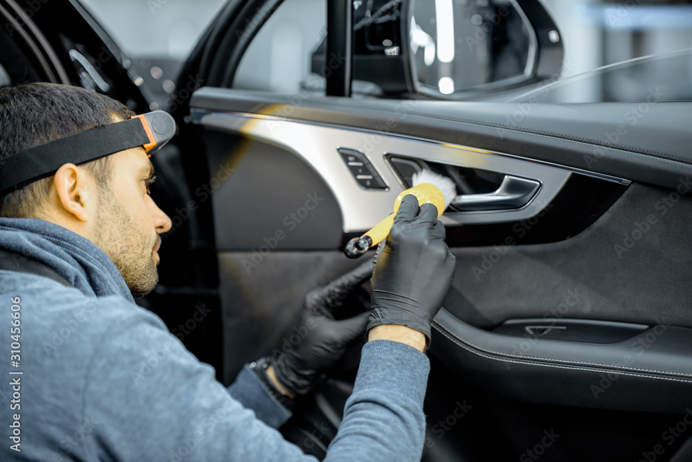 Car service worker in uniform provides a professional vehicle interior cleaning, wiping door panel w