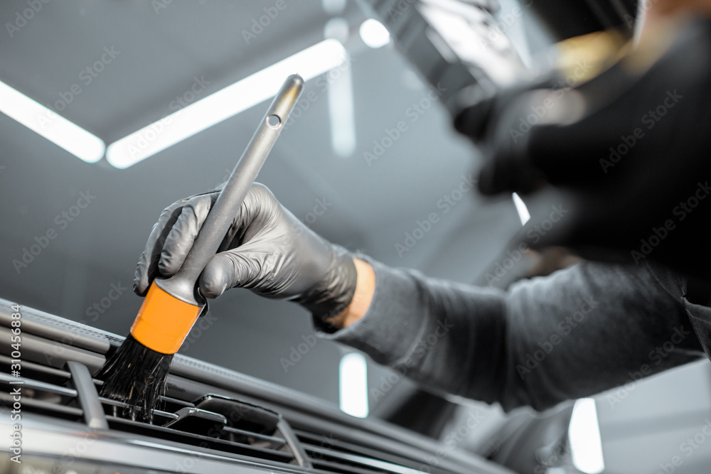 Worker provides a professional vehicle interior cleaning, wiping indoor front panel with a brush at 