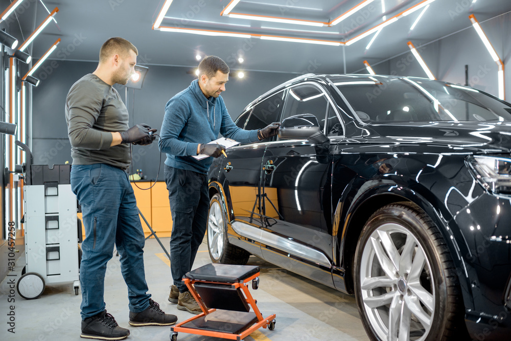 Two car service workers examining vehicle body for scratches and damages while taking a car for prof