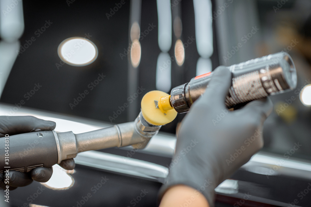 Worker in protective gloves applying wax on a grinder for car body polishing, close-up. Professional