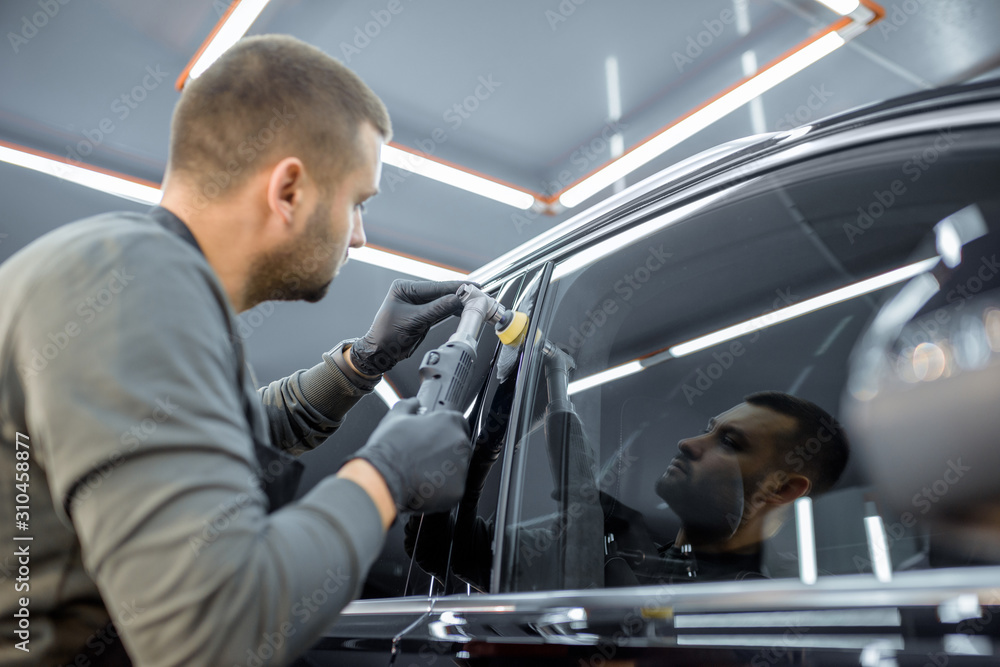 Car service worker polishing vehicle body with special wax from scratches. Professional car detailin